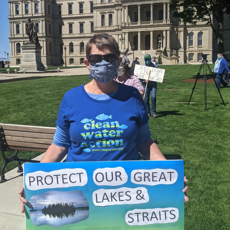 Protestor holding sign saying: "Protect Our Great Lakes &amp; Straits, Shut Down Line 5 Now" in front of the MI state capitol building