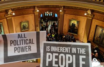 Michigan Capitol Rotunda, crowd with sign in foreground: All Political Power Is Inherent In The People